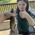 Jack smiling while holding a fish beside the water